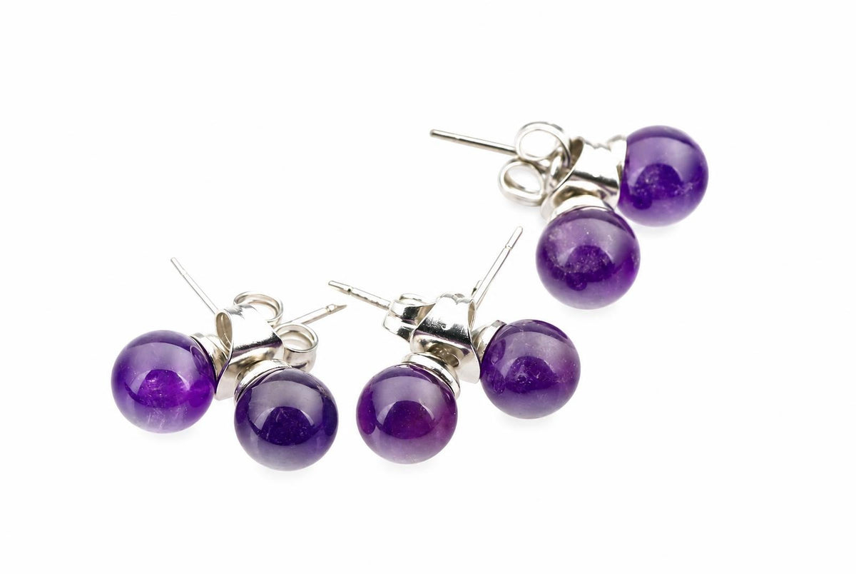 Dvi sidabriniai auskarai su violetinėmis sferinėmis ametišto akmenimis ant balto fono.