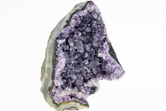 Iškirptas ametisto gabalas su violetinėmis ir baltais kristalais bei pilkšva ruda išorine danga ant baltos fono.