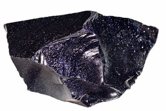 Tamsiai mėlynas, blizgus mineralinis gabalas su žvaigždžių efektu ant balto fono.
