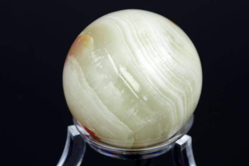 Oniksas sfera – 35mm natūralus poliruotas kristalas su unikaliomis linijomis ir švelniu baltu bei rusvu atspalviu, tinkantis meditacijai ir namų dekoracijai.