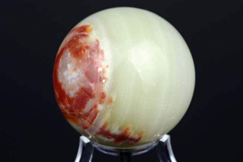 Oniksas sfera – 50mm poliruota natūralaus onikso kristalo sfera su šviesiai žalios ir raudonos spalvų deriniu bei unikaliu raštu, idealiai tinkanti meditacijai ir dekoracijoms.