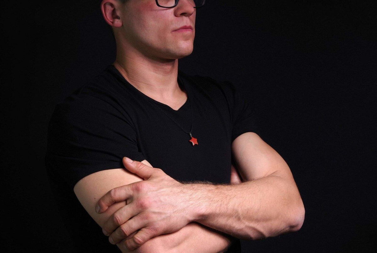 Vyras juodoje aprangoje dėvi Raudonas jaspis pakabukas – Žvaigždutė, natūralus pusbrangis akmuo su unikaliu, žvaigždės formos dizainu ant kaklo.