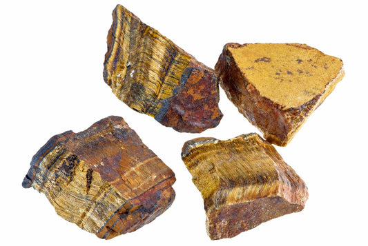 Keturi neapdirbti tigro akies mineralo gabalai su geltonomis, raudonomis ir tamsiomis juostelėmis ant baltos fono.