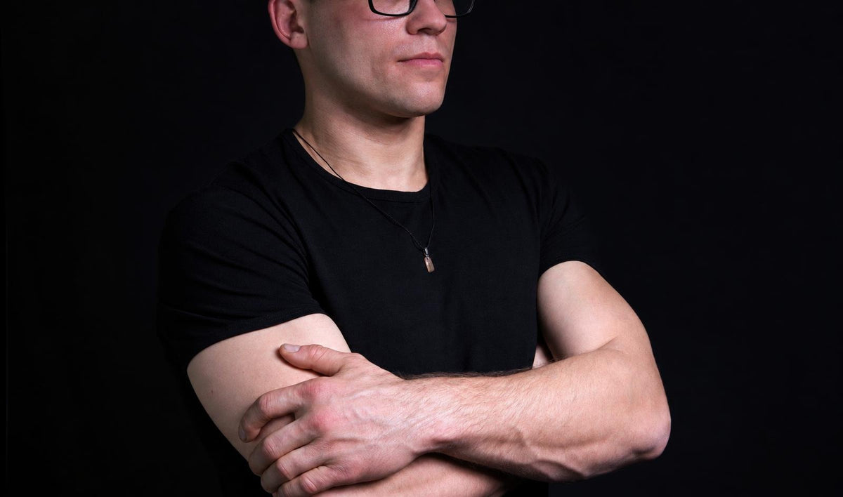 Vyras juodu marškinėliu su tamsiu fone, dėvintis geltoną pakabuką ant kaklo.