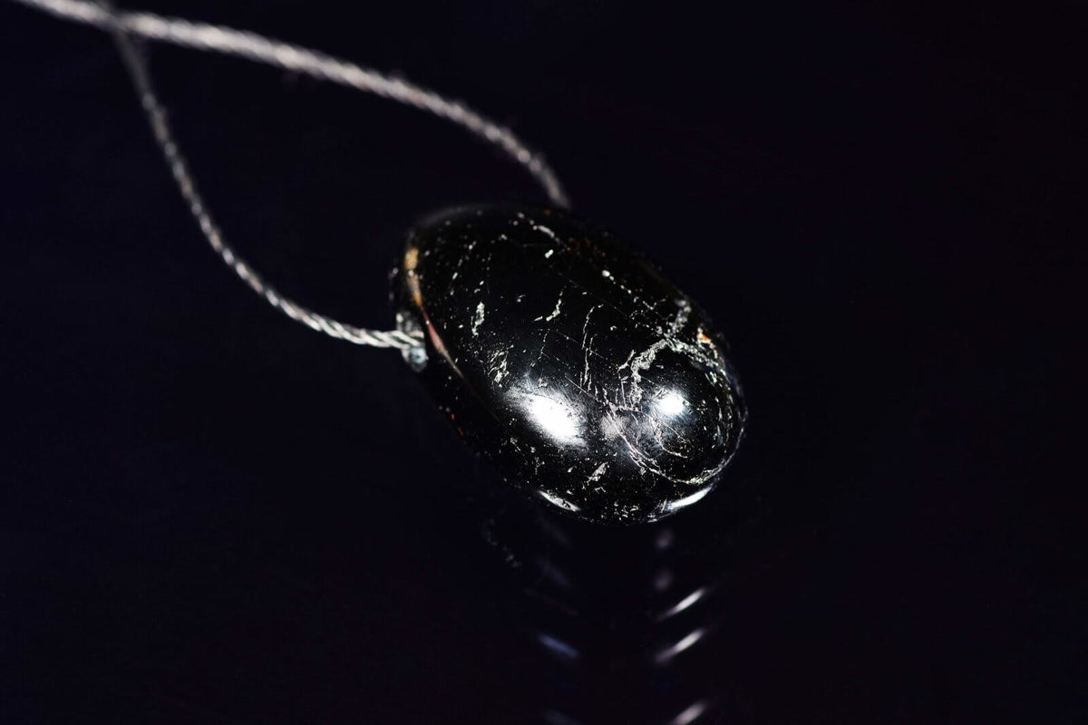 Juodas blizgus akmuo su matinėmis baltomis įtrūkimų linijomis ant plonos grandinėlės, rankų darbo kristalų papuošalas Turmalinas pakabukas – Lašas.