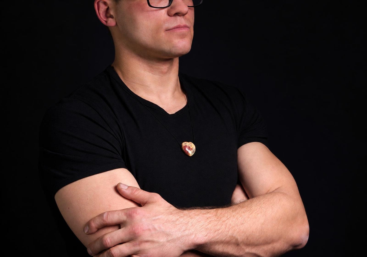 Vyras juodu marškinėliu dėvi kaklo pakabą su širdies formos agato akmeniu ant tamsaus fono.