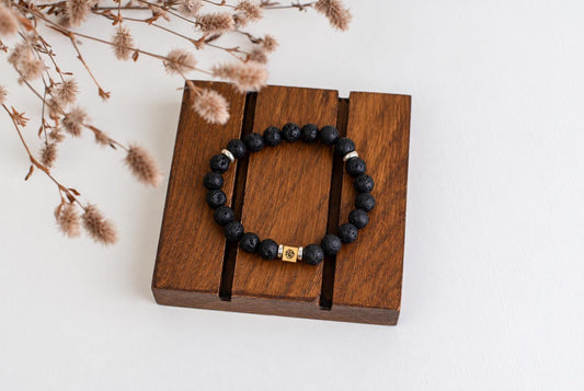 Juoda lava apyrankė su sidabriniais ir auksiniais akcentais ant medinio stalo.