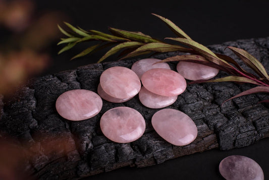 Rūkytas tamsus medis, ant kurio išdėstyti rožiniai kvarciniai delninukai ir žalios bei raudonos spalvos lapų šaka.