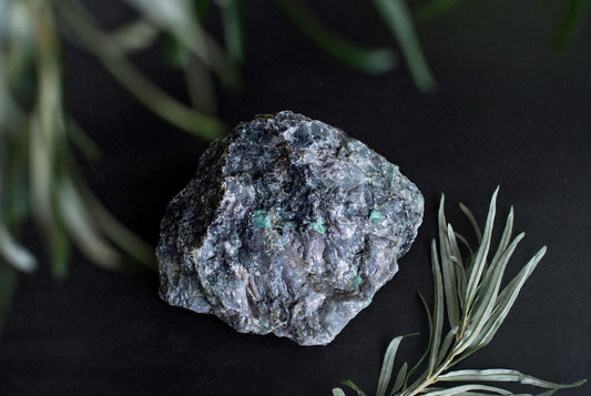 Didelis, šiurkštus mineralinis akmuo su tamsiai pilkomis ir žaliomis dėmėmis ant juodos fono.