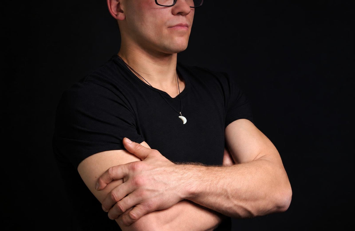 Vyras juodu marškinėliu dėvi pakabuką su balta, mėnulio formos detalėmis ant kaklo.