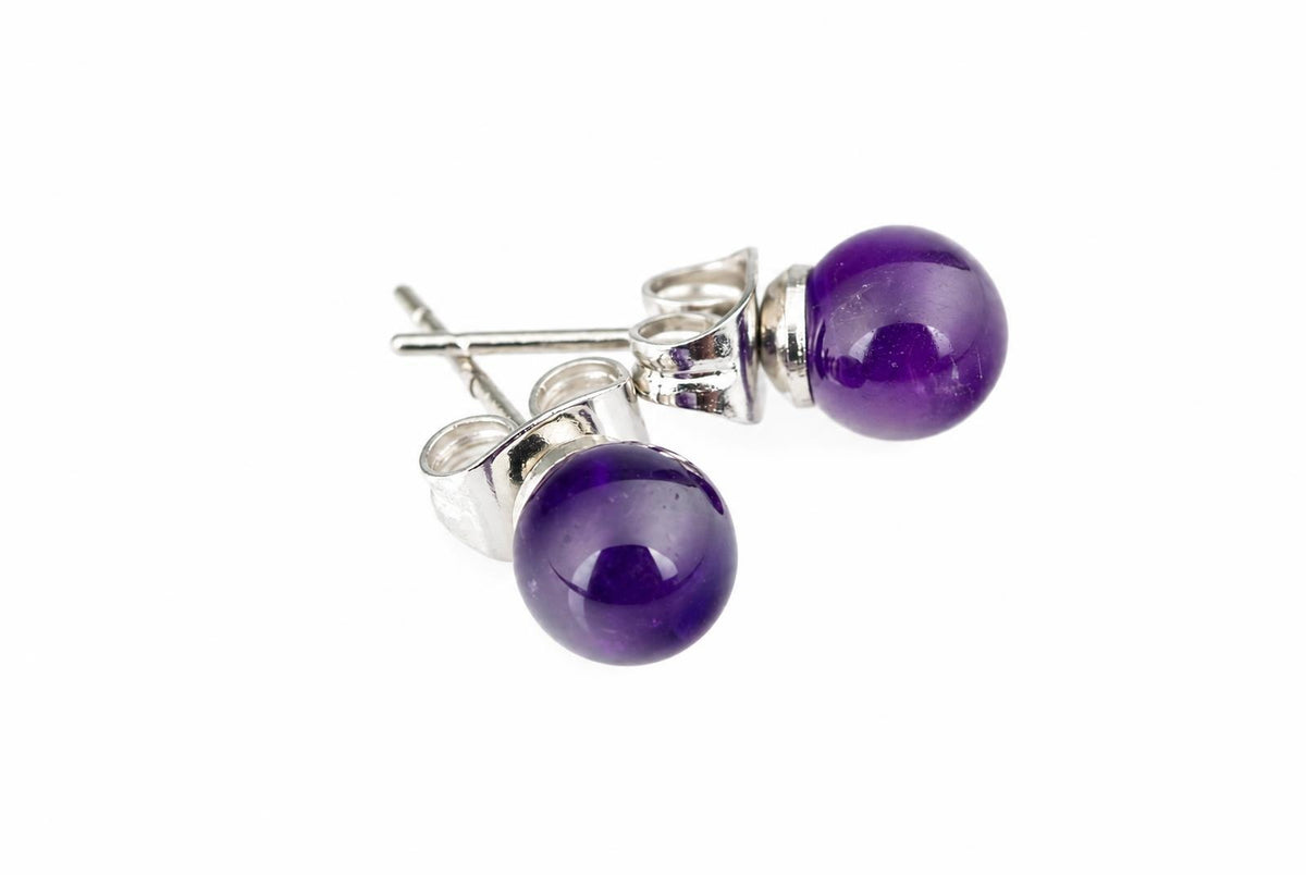 Dvi sidabriniai auskarai su apvaliais tamsiai violetiniais akmenimis ant balto fono.