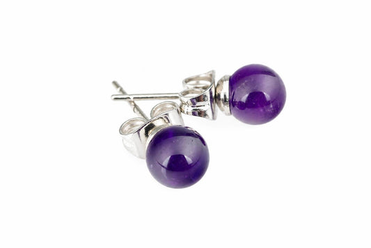 Dvi sidabriniai auskarai su apvaliais tamsiai violetiniais akmenimis ant balto fono.