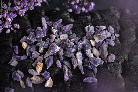 Tamsiame fone išdėstyti violetiniai ir pilki neapdirbti ametisto kristalai su saulėgrąžų žiedais.