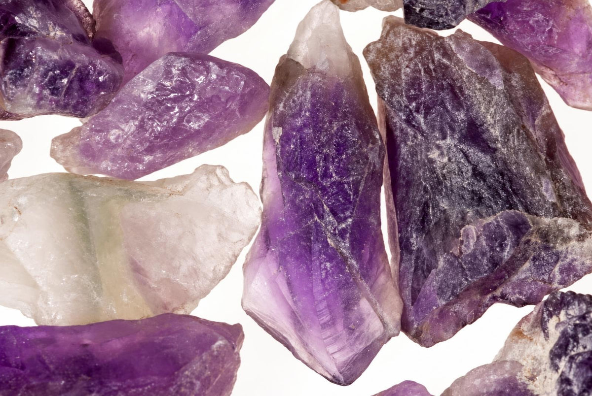 Kelių ametistų kristalų gabaliukai su violetinėmis ir baltomis dalytėmis ant balto fono.