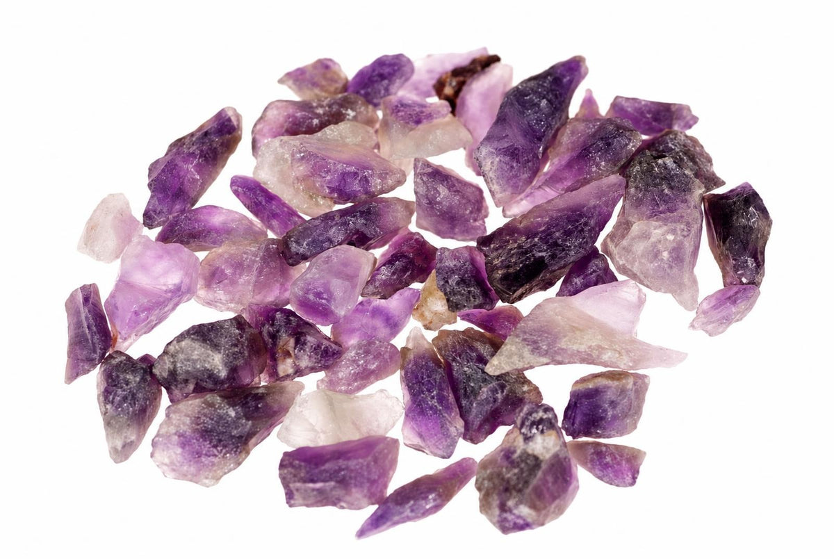 Neapdirbtų violetinių ir šviesių ametisto gabalėlių krūvelė baltame fone.