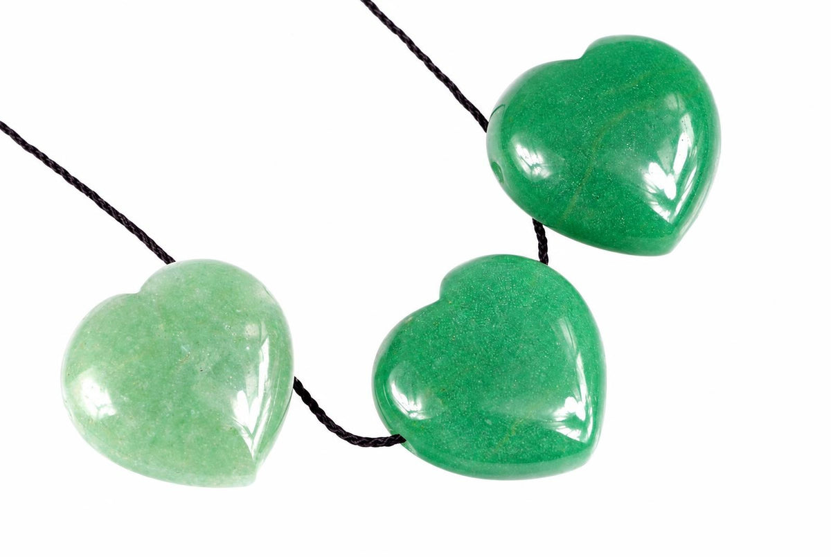 Trys šviesiai žalios, širdies formos pakabukai ant tamsaus virvelės, išdėstyti baltame fone.