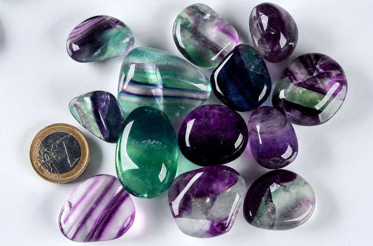 Keliolios poliruotos fluorito akmenų kolekcija su violetinėmis, žalios ir baltos spalvos juostomis bei viena eurais.