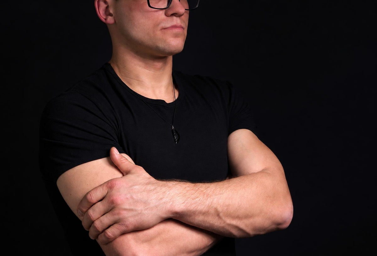 Vyras juodu marškinėliu dėvi pakabuką su juodos spalvos, sparno formos detalėmis ant kaklo.