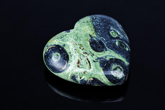 Poliruota širdies formos akmuo su žalia ir tamsiai mėlyna spalva bei apskritais raštais ant juodos, atspindinčios paviršiaus.