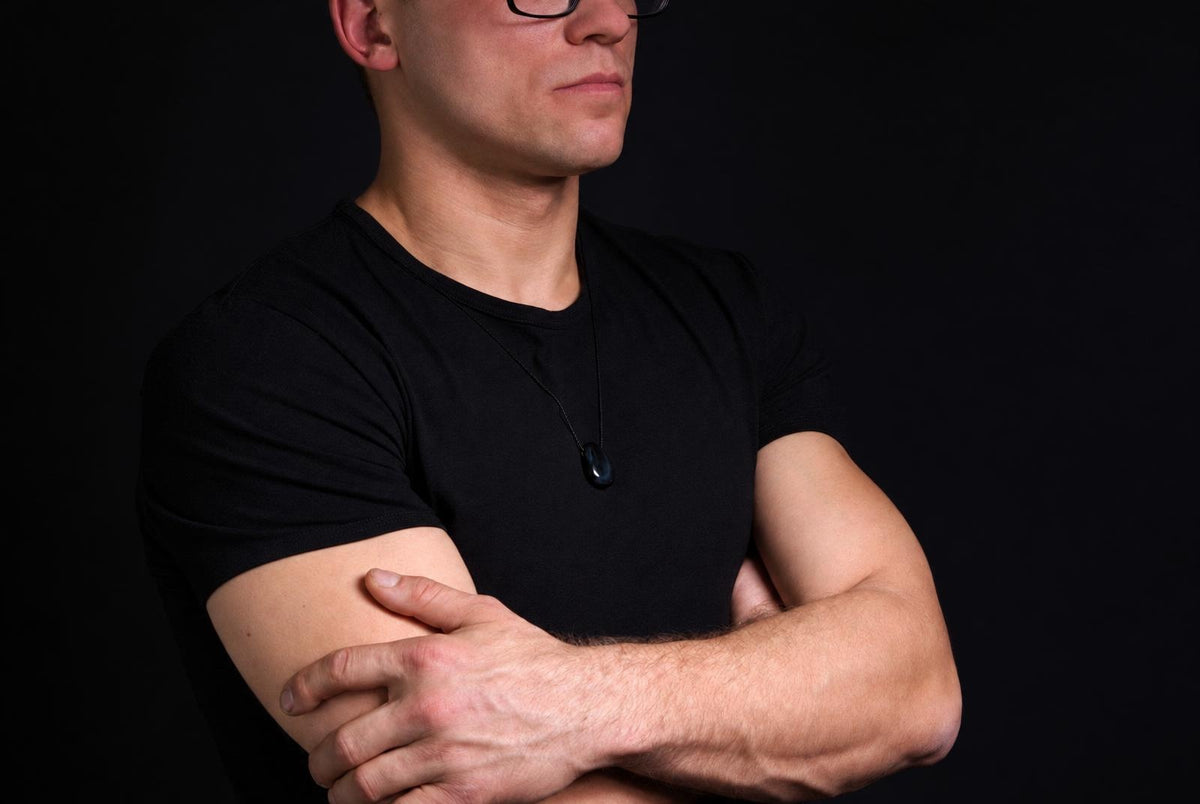 Vyras juodais marškinėliais dėvi tamsų mėlynosios tigro akies lašo formos pakabuką ant juodos virvelės.