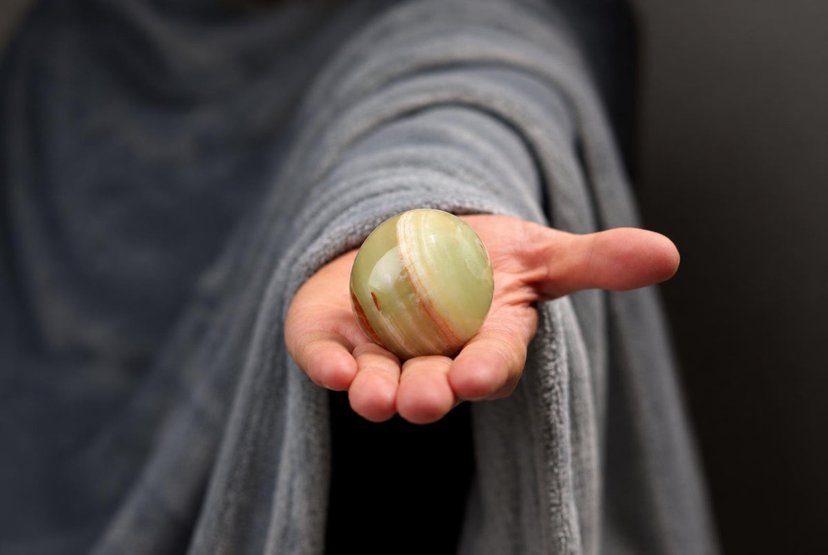Ranka laiko apvalų, šviesiai žalią ir raudonai juostuotą akmenį ant tamsaus fono.