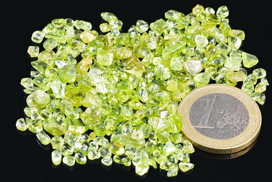 Žalių peridotų akmenų grupė ant tamsaus paviršiaus su vienu euru.