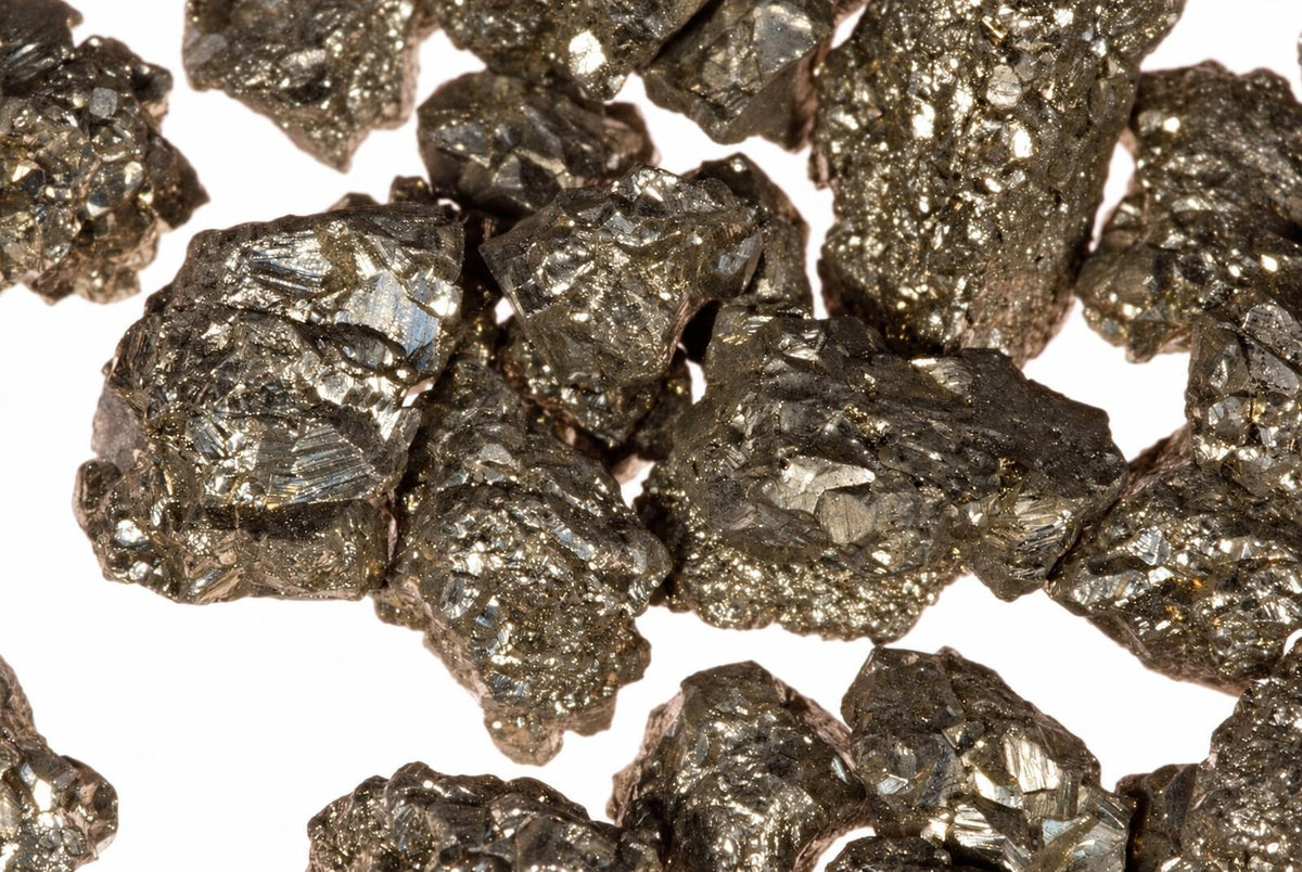 Keli plokšti, blizgūs tamsiai pilki mineralų gabalėliai su šviesiais atspindžiais ant baltos fono.