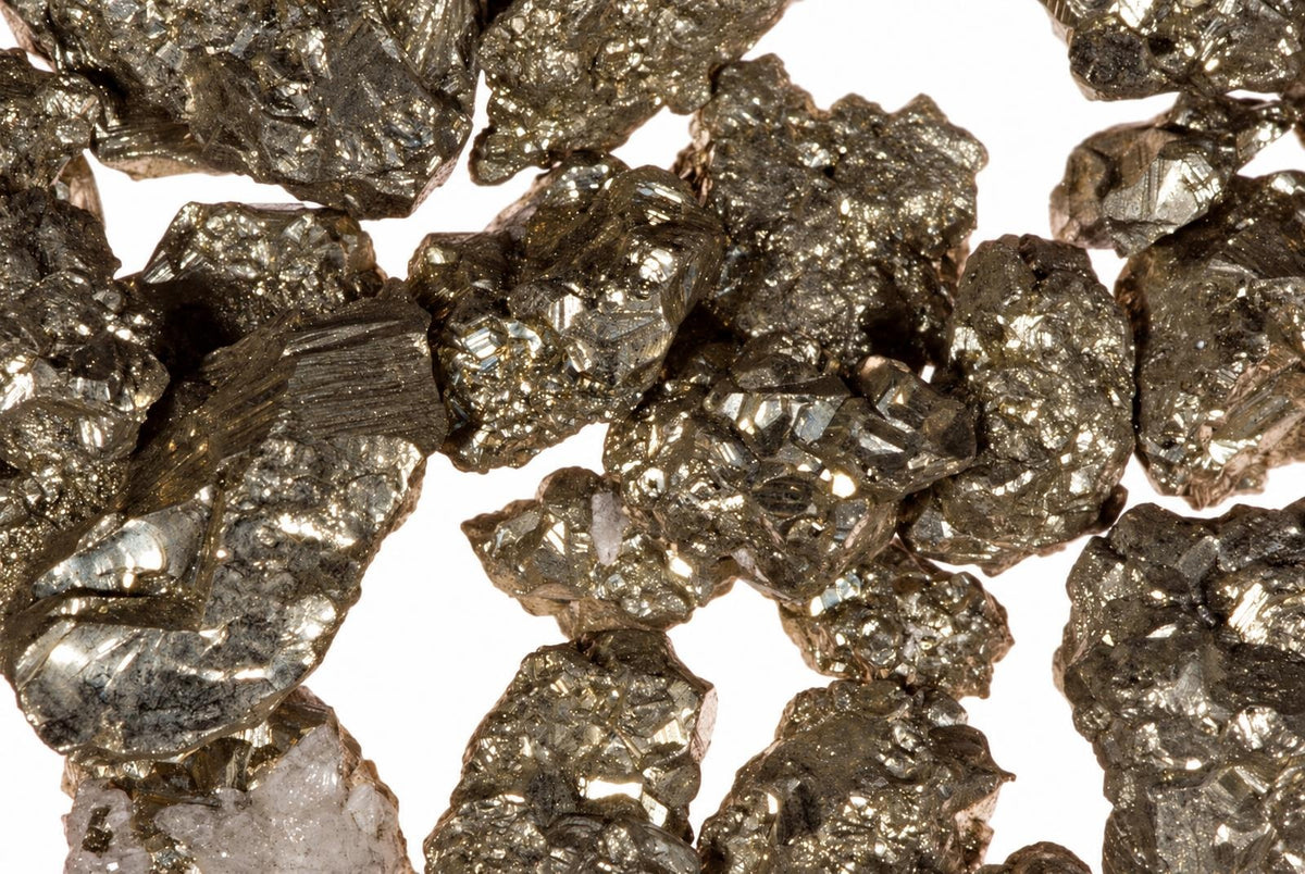 Kelių plokščių, blizgančių, tamsiai pilkų ir auksinių atspalvių mineralų gabaliukai ant baltos fono.