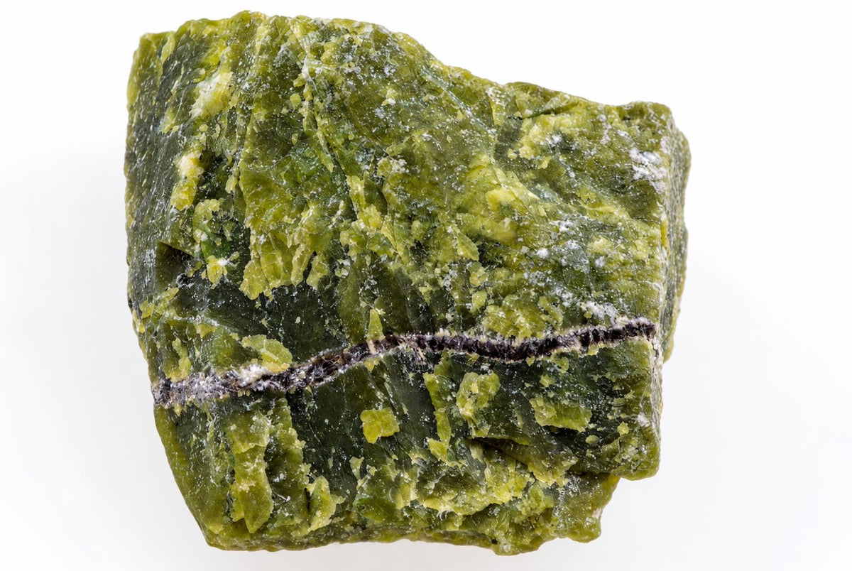 Žalia, neapdirbtas mineralinis akmuo su tamsia juosta ir baltomis dėmėmis ant balto fono.