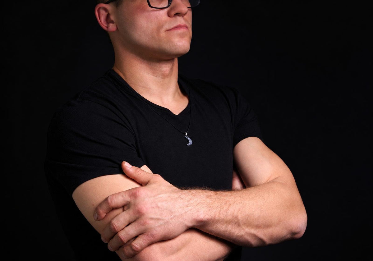 Vyras juodu marškinėliu dėvi pakabuką su mėnulio formos, sidabrinės spalvos detalėmis ant kaklo.