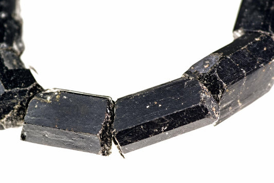 Apyrankė su juodais, neapdirbtų turmalino kristalų gabalais ant balto fono.