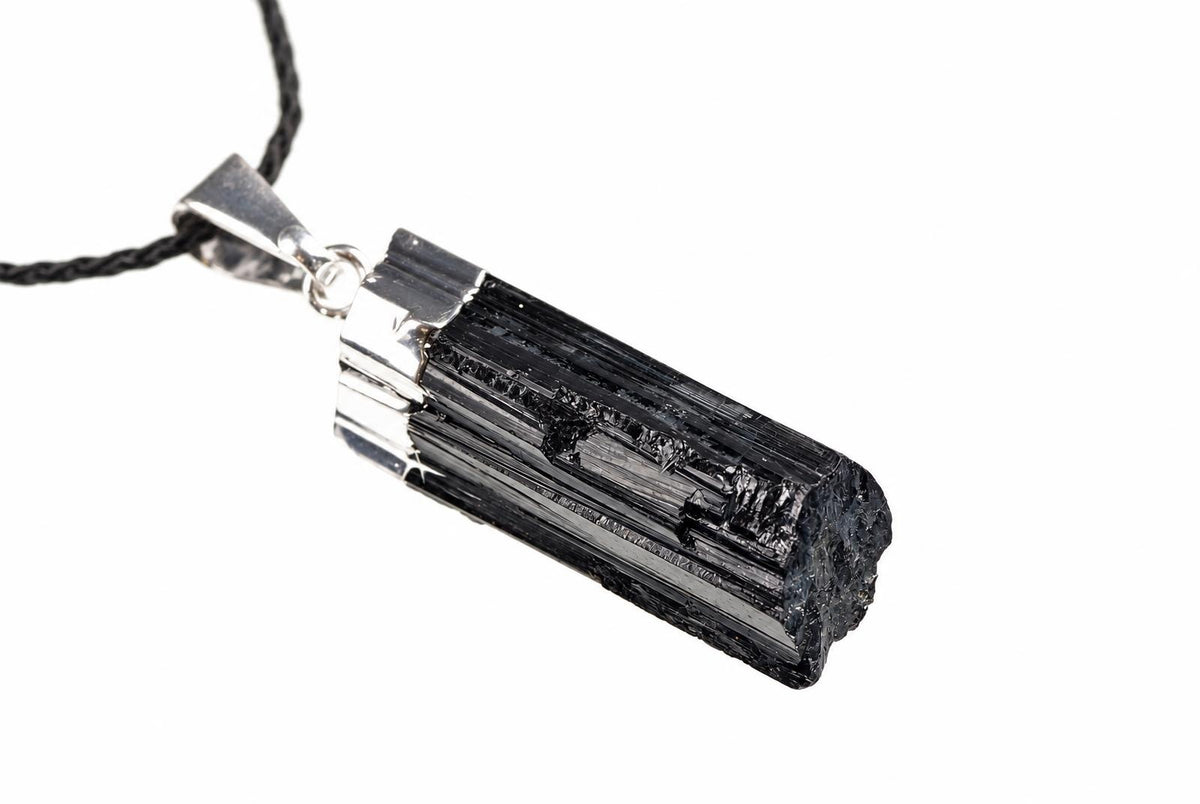 Juodo turmalino šerlo pakabuko detalė su išilginėmis rievėmis ir metaliniu tvirtinimu baltame fone.